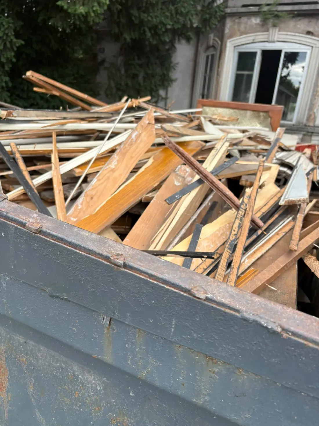 Benne chargée de bois de charpente et de lattes claires devant une maison ancienne